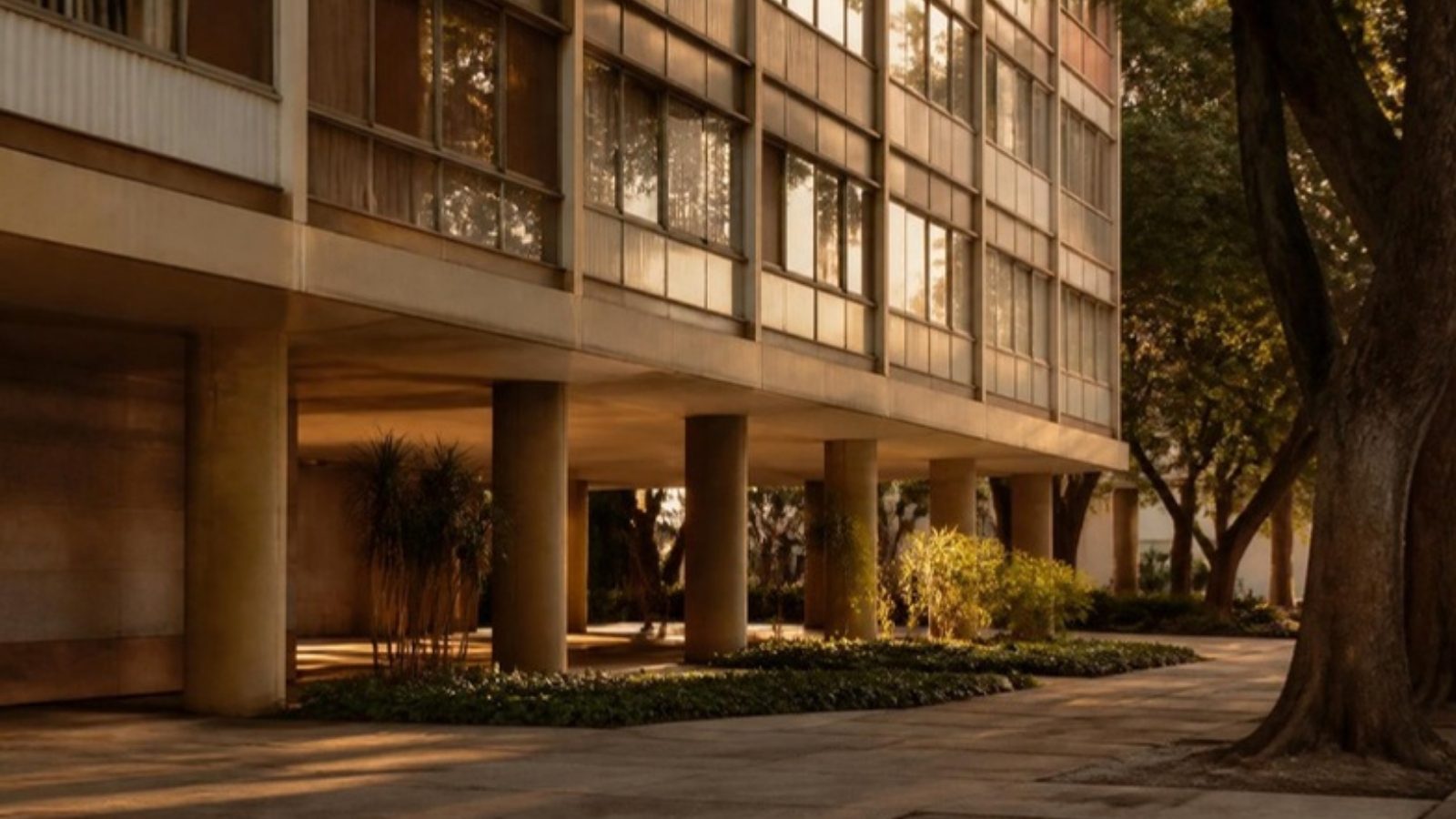 Edifício residencial modernista de Brasília com pilotis e árvores ao entardecer